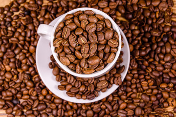 White cup filled with coffee beans on wooden table. Top view