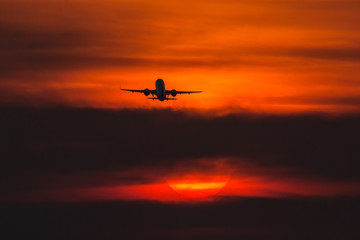 Air plane taking off at sunset near to the sun with beautiful red cloud in background