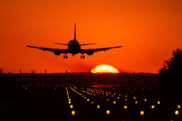 Silhouette of air plane landing on illuminated track at sunset with beautiful red sky and sun in...