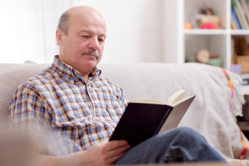 Senior man reading a book on his sofa