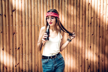 So delicious! Stylish cute girl in red bandana is drinking soda using a straw, isolated on bright wooden background, copy space. Lifestyle,trendy concept.