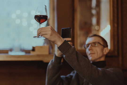 Photo with shallow depth of field, toned and stylized as a film of a man making photo with phone of glass of red wine in hand for his social media account