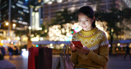Obraz premium Woman look at mobile phone in city with shopping bag at night