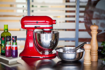 Red professional mixer surrounded by spices and olive oil stands on a metal table