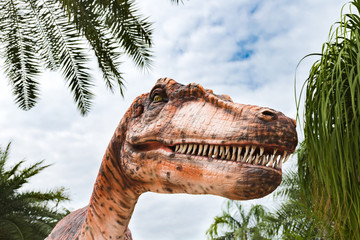 Close up on a realistic statue of Tyrannosaurus in dinosaur park. T-Rex head with sharp teeth against blue sky.