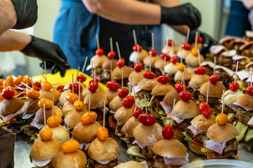 Female and Male Chef Putting Ingredients of Burgers on a Sliced Bread Spread on a Table in Black Gloves