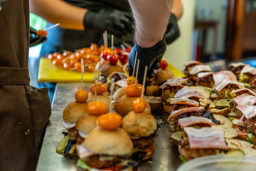 Female and Male Chef Putting Ingredients of Burgers on a Sliced Bread Spread on a Table in Black Gloves