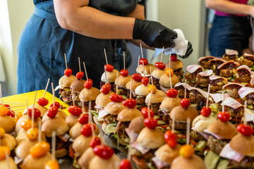 Female and Male Chef Putting Ingredients of Burgers on a Sliced Bread Spread on a Table in Black Gloves