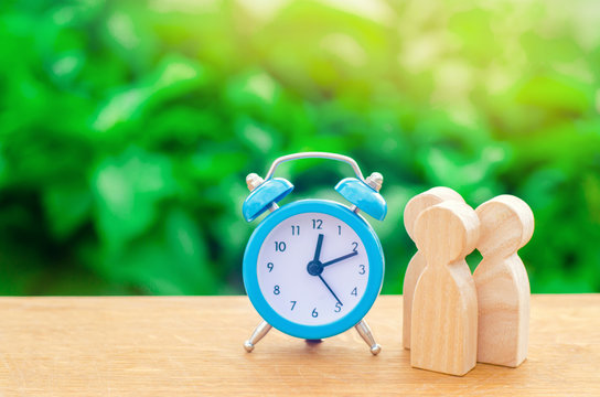 Three wooden human figures standing near a blue alarm clock on a green background. The concept of hopes and expectations. Queue. Planning. Business, minimalism. Friends and family - Powered by Adobe