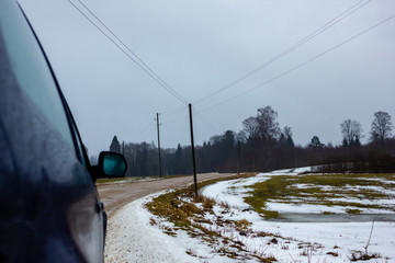 Empty Countryside Landscape in Cloudy Winter Day with Snow Partly Covering the Ground and Fog - Part of the Car in the Foreground