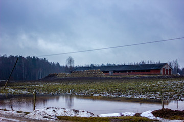 Empty Countryside Landscape in Cloudy Winter Day with Snow Partly Covering the Ground and Fog, Old Farm in the Background