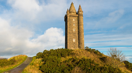 Panoramic view of a path leading to an old hilltop castle tower under a blue sky with white puffy clouds - Powered by Adobe