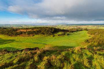 Fototapeta na wymiar Eary morning golden hour light reveals a lush green golf course with a rolling landscape of grass and fields in the distance on the Ards Peninsula, County Down, Northern Ireland
