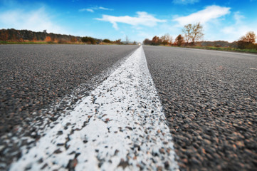 Close-up of a traffic line on an empty road with a forest and sky with clouds on the background