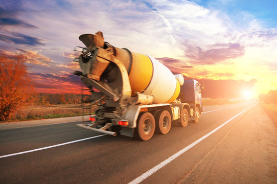 Concrete mixer truck on the countryside road against sky with sunset
