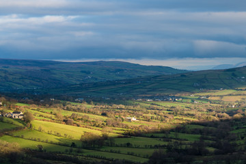 Bright sunlight breaking through clouds highlights a beautiful lush green landscape of farms and fields in Glenariff, County Antrim, Northern Ireland