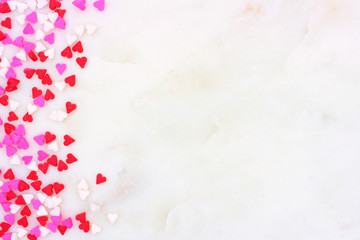 Valentines Day candy heart sprinkles side border over a white marble stone textured background