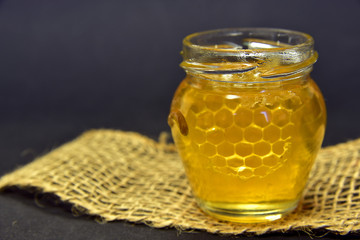 honig im glas mit bienenwabe vor dunklem hintergrund