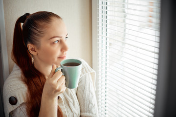 drinking tea sitting on the window of Caucasian beautiful middle-aged woman with red hair