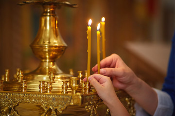 mother and daughter light candles in the Orthodox Church, close-up of hands