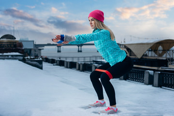 Sporty woman squatting doing sit-ups with resistance band outdoor in winter. Strength and...