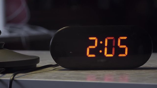 View of black plastic rectangular shaped electronic digital clock showing time in orange color and placed on grey table.