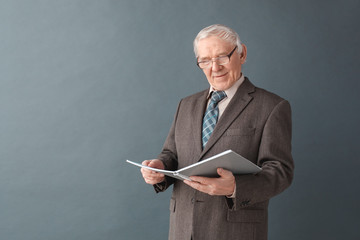 Senior man teacher wearing glasses studio standing isolated on gray reading journal concentrated