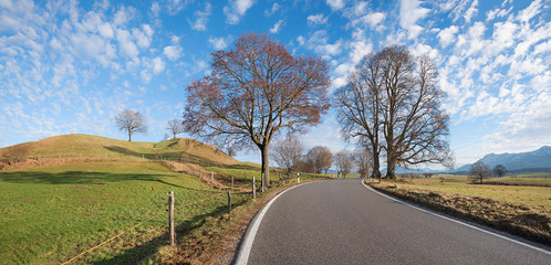 Landstraße im Voralpenland, ländliche Gegend mit Hügeln und blauer Wolkenhimmel