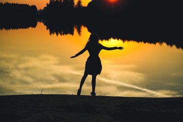 Silhouette of a young beautiful girl in a jump on a background of a sunset in reflection pond