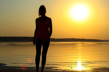Silhouette of a young beautiful girl walking along the seashore during orange sunset
