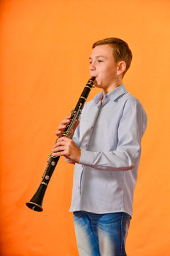 The boy performs solo at a concert, plays the clarinet on an orange background.