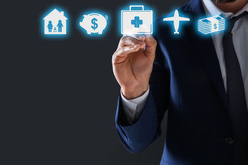 Businessman choosing icon on virtual screen against dark background. Life and health insurance