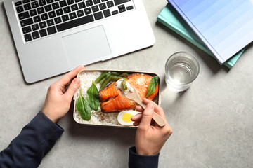 Woman eating natural protein food from container at office table, top view