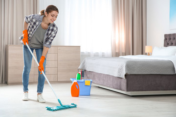 Young woman washing floor with mop in bedroom, space for text. Cleaning service