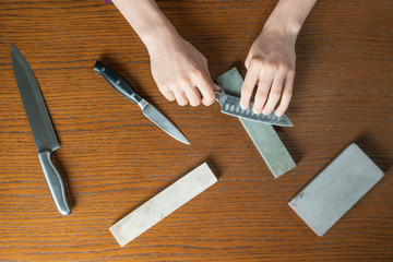 young man sharpening a knive on wooden table on dark background b