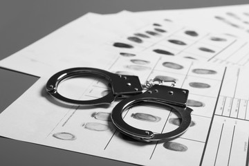 Police handcuffs and criminal fingerprints card on table, closeup