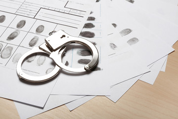 Police handcuffs and criminal fingerprints card on wooden background, space for text