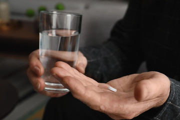 Senior man holding pill and glass of water indoors, closeup