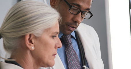 Closeup of two doctors consulting with each other inside medical office. Tight shot of male black doctor talking to senior medical colleague