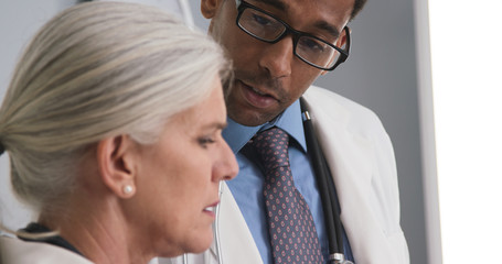 Closeup of two doctors consulting with each other inside medical office. Tight shot of male black doctor talking to senior medical colleague