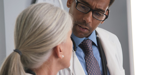 Closeup of two doctors consulting with each other inside medical office. Tight shot of male black doctor talking to senior medical colleague