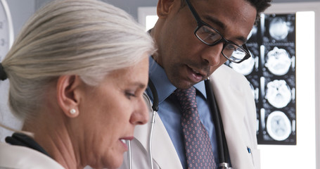 Male radiologist consulting with senior colleague about patients ct scans. Close up of millennial doctor reviewing patient medical record with senior assistant