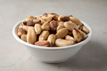 Bowl with tasty Brazil nuts on grey background