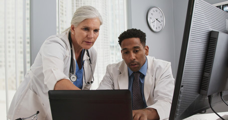 Female caucasian senior doctor working with young african-american colleague on laptop computer. Close up of two medical professionals working together with technology inside office