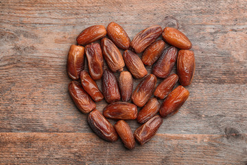 Heart shaped pile of sweet dried date fruits on wooden background, top view