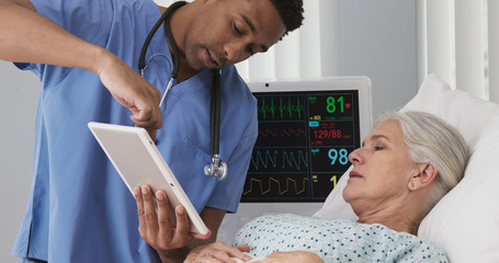 Male registered nurse using tablet to show senior woman test results from her surgery. Elderly...