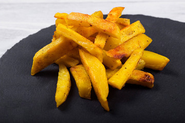 Fried French fries on a black slate plate, wooden background