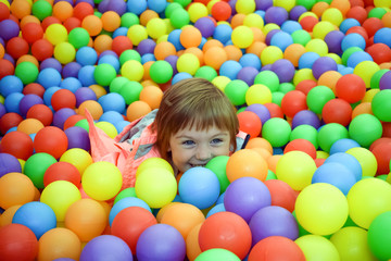 Fototapeta na wymiar The child is a part of plastic balls. The girl is playing and having fun. The concept of a happy, carefree childhood. Entertainment and recreation with children.