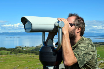 Fototapeta na wymiar A man looks at the panoramic binoculars from the top of the hill. View of the sea. Blue sky. Sunny day.