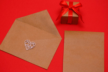 Valentine's Day, February 14th a figured, wooden, white heart on an envelope on a red background, next to a gift in a package tied with a red ribbon, a holiday concept, a cardboard sheet for writing